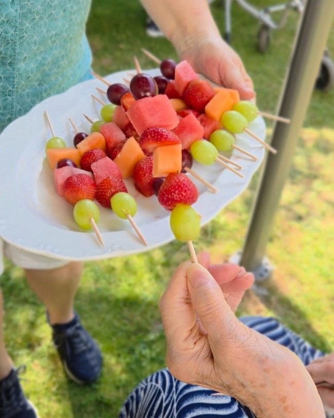 Ein Teller mit bunten Obstspießen wird einer Bewohnerin hingehalten.
