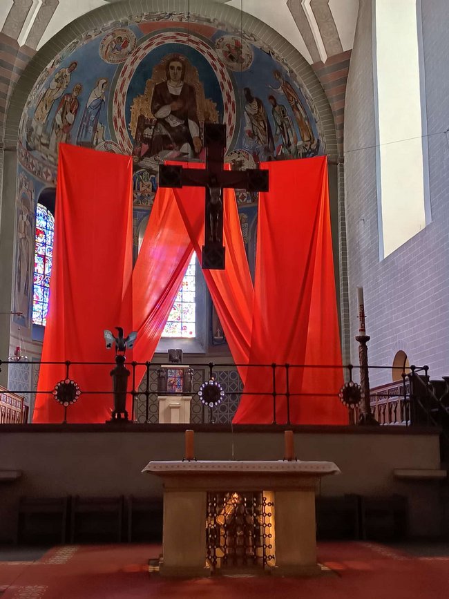 Blick auf den Altar mit Kreuz und wallenden orangefarbenen Tüchern.