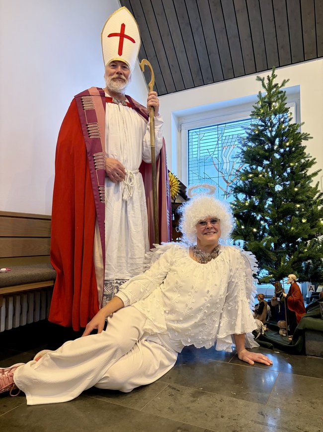 Der Nikolaus und seine himmlische Begleiterin posieren in der Kapelle vor Krippe und Tannenbaum.