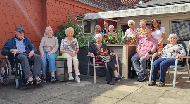 Gäste der Tagespflege posieren mit zwei Mitarbeiterinnen vor dem Hochbeet.
