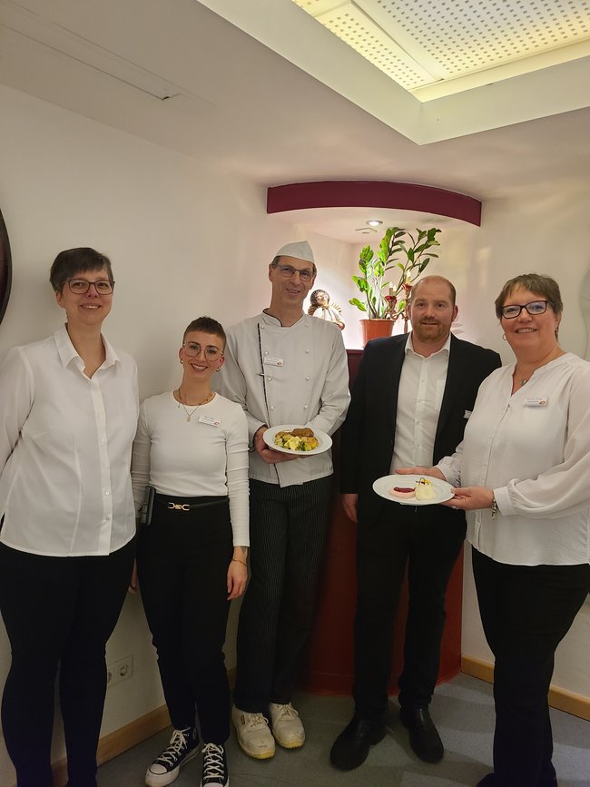 Das Küchenteam, Einrichtungs- und Pflegedienstleitung sowie Leitung Sozialer Dienst präsentieren das Menü auf Tellern.