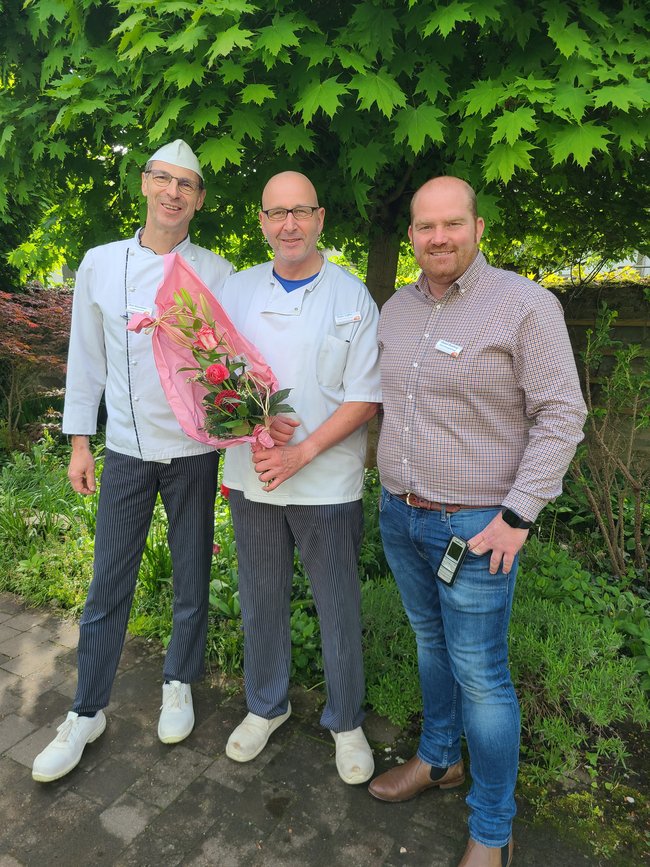Einrichtungsleiter Daniel Romberg (rechts) und Hauswirtschaftsleiter Dirk Hanemann (links) gratulieren Stefan Löffler (Mitte) zum 25-jährigen Dienstjubiläum und überreichen einen Blumenstrauß.