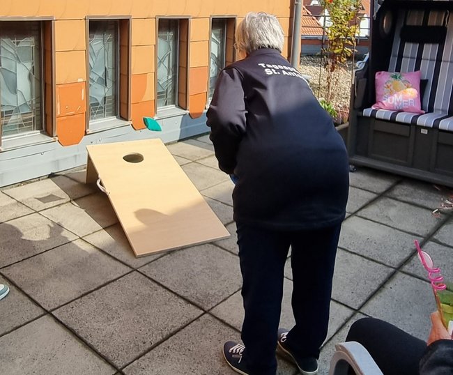 Tagespflegegast wirft Säckchen auf Holzbrett.