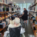 Zwei Seniorinnen schauen sich mit ihrer Begleiterin die Regale und Bücher an.