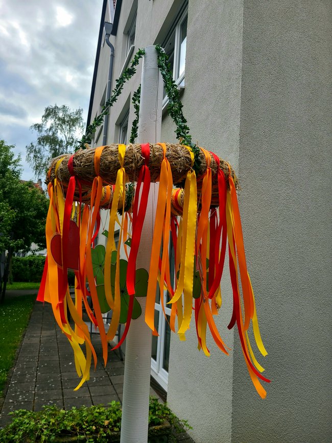 Der Maibaum im Garten erstrahlt in den Farben gelb, orange, rot.