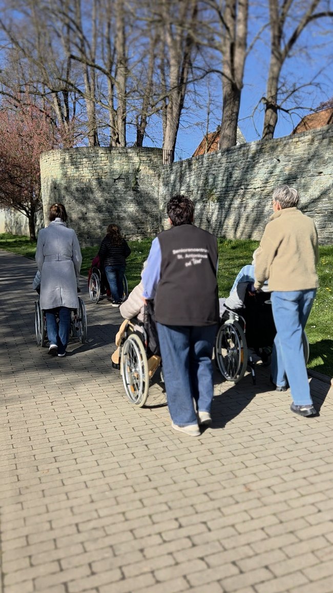 Bewohner im Rollstuhl sind mit den Mitarbeiterinnen spazieren an der Soester Gräfte.