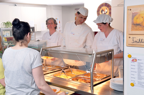 Mitarbeiter der Hauswirtschaft geben Essen am Buffet aus.